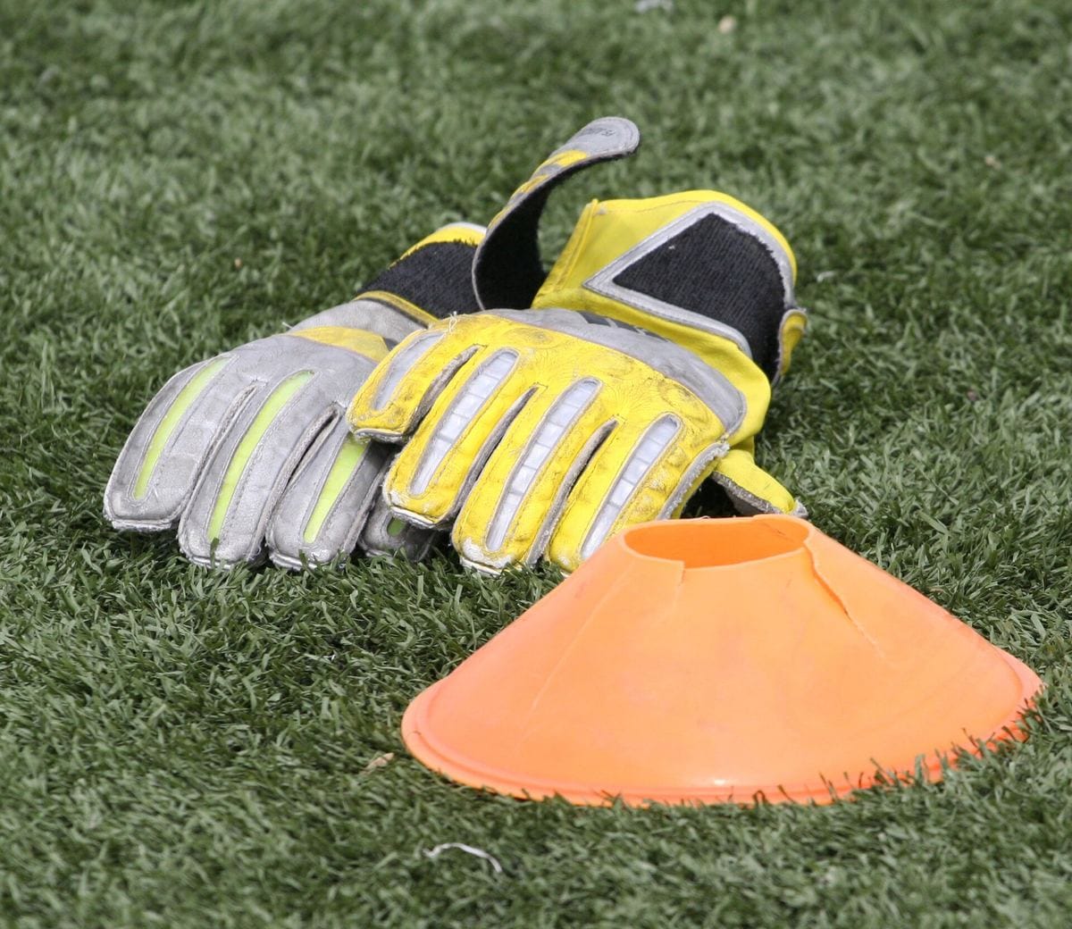 Goalkeeper gloves and a training cone on a grass pitch